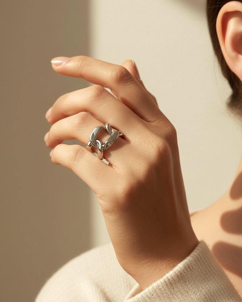 A close-up studio shot of a chunky, adjustable silver-tone ring on a plain white or light beige background. The ring has a bo