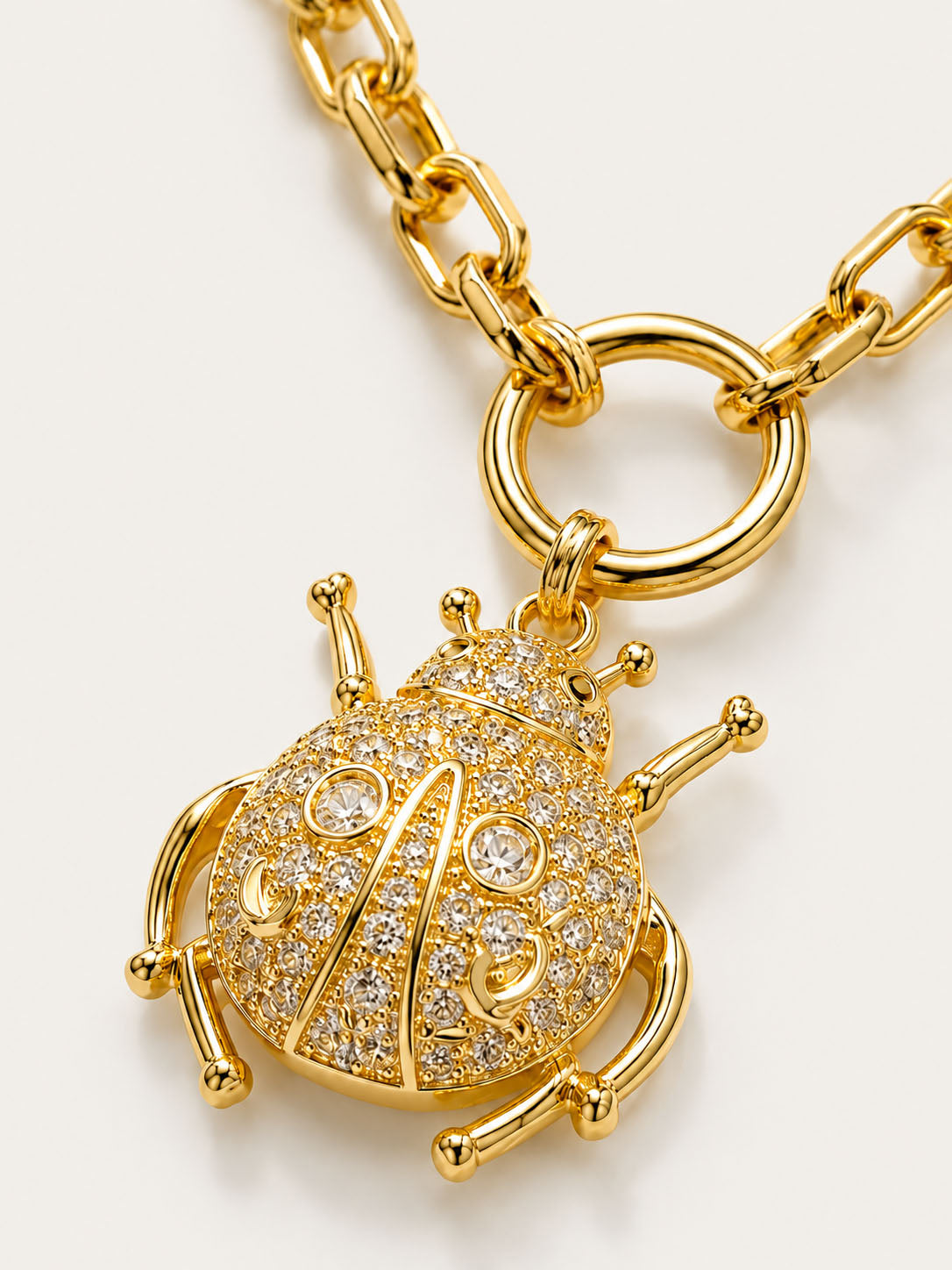 Gold beetle-shaped charm with 'AB' initials on a gold chain against a white background