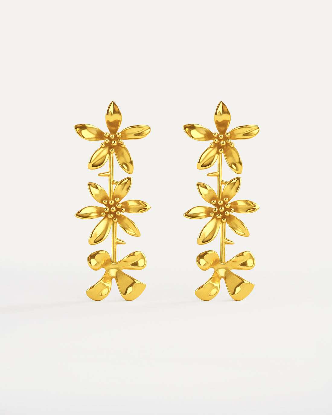Gold-plated cascading flower drop earrings featuring three dimensional daisy designs stacked vertically, measuring 79mm in length with delicate petal details