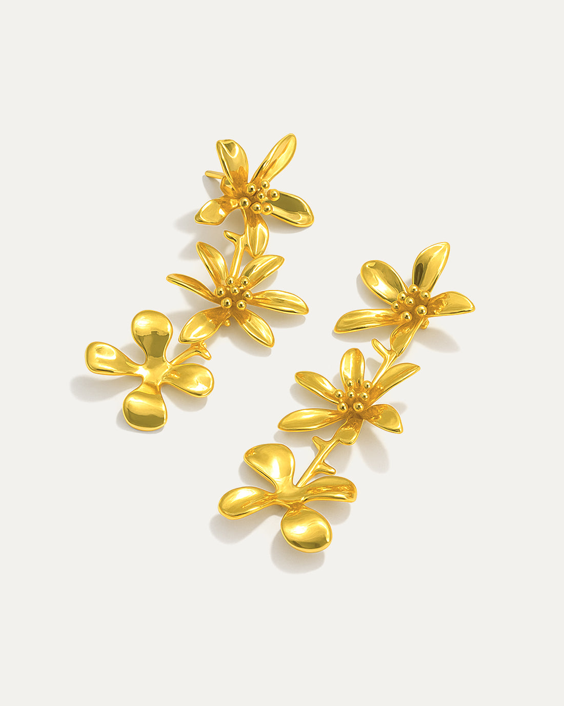 Gold-plated cascading flower drop earrings featuring three dimensional daisy designs stacked vertically, measuring 79mm in length with delicate petal details