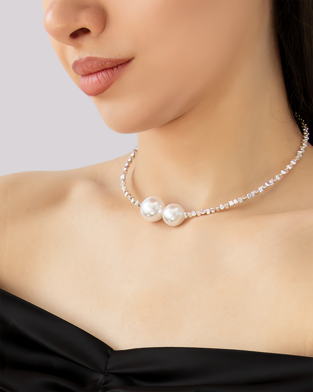 Close-up of a pearl choker necklace featuring two oversized faux pearls and a silver-tone beaded strand, worn on a woman's neck.