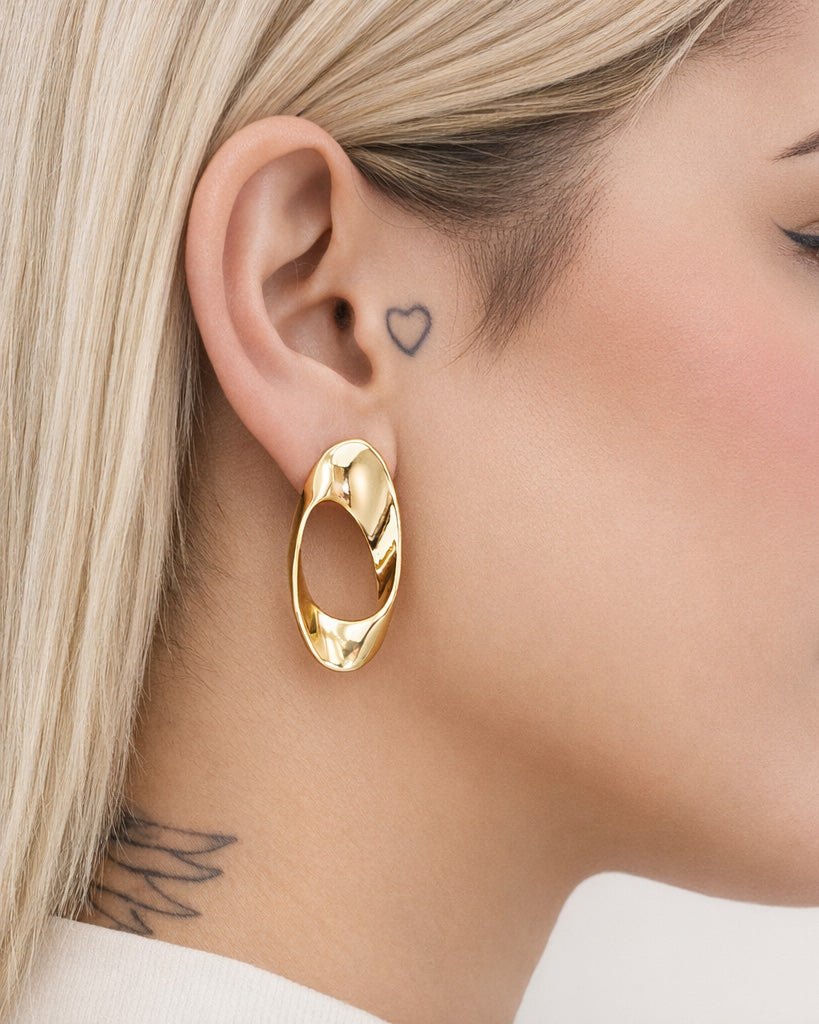 Modern asymmetric gold-plated hoop earrings with twisted oval design and hollow center, featuring a high-polish finish and contemporary sculptural shape