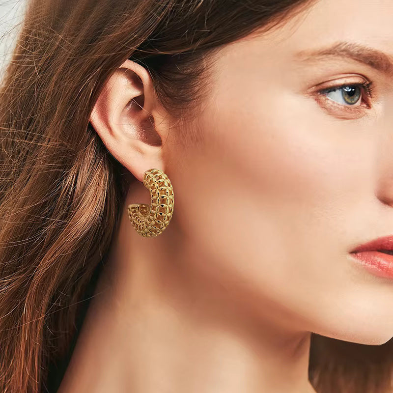 Gold hoop earrings with intricate design on a light beige background