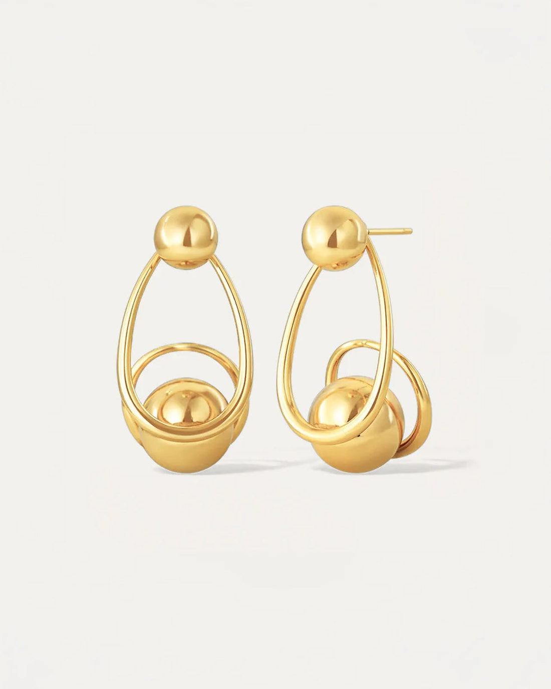 Gold sculptural drop earrings with overlapping loops and sphere accents, worn on model.