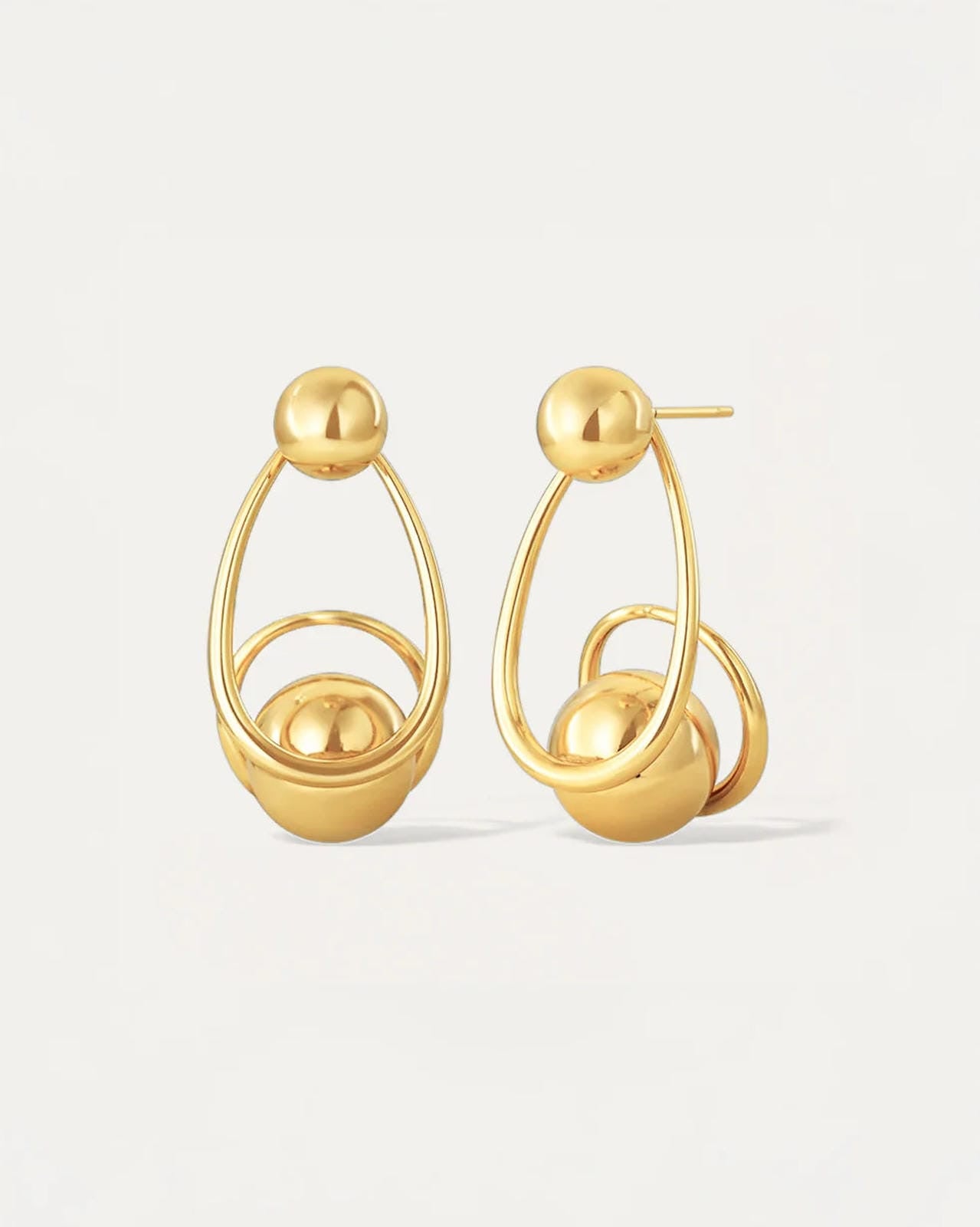 Gold sculptural drop earrings with overlapping loops and sphere accents, worn on model.
