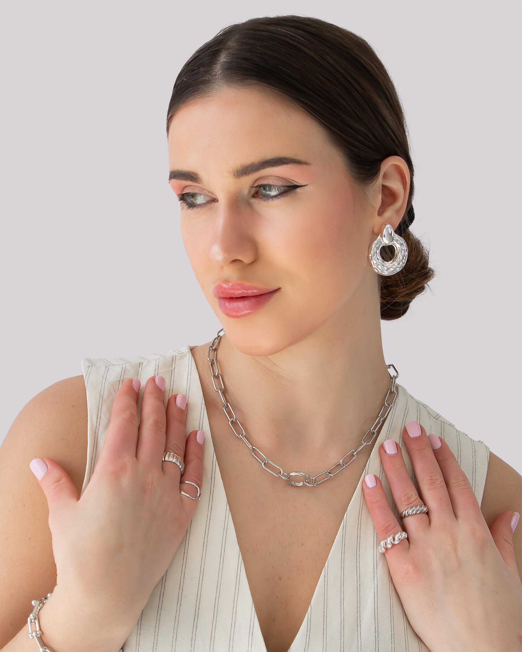 Model wearing silver sculptural hammered oval drop earrings with open center – high-shine statement design.