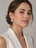 Close-up of a person wearing silver heart-shaped earrings with a textured ball on a neutral background