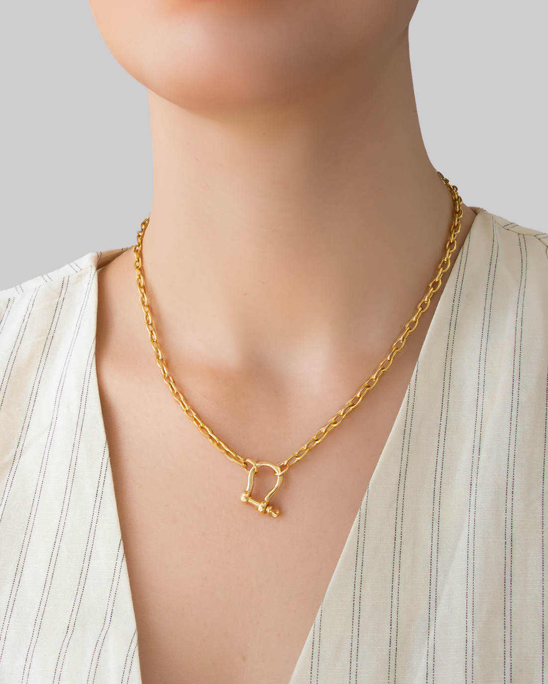 Gold chain necklace with bold D-shackle pendant worn with light striped fabric.
