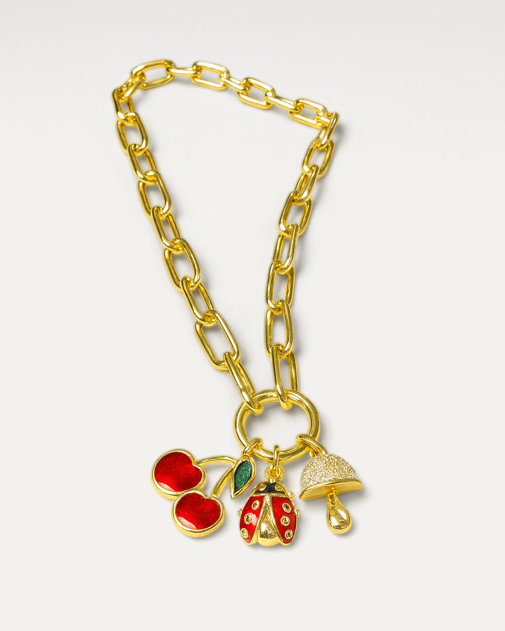 Gold chain bracelet with red cherry, ladybug, and baby pacifier charms on a white background