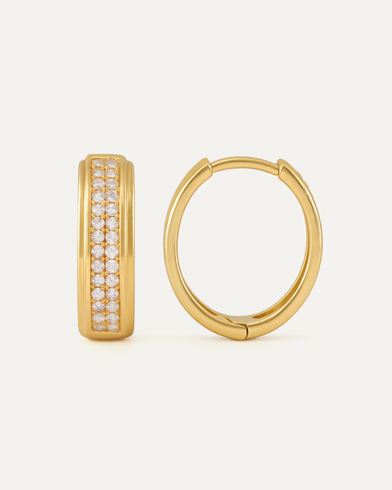 Gold hoop earrings with embedded stones on a light beige background