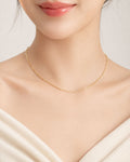 Gold necklace on a person wearing a white top against a neutral background