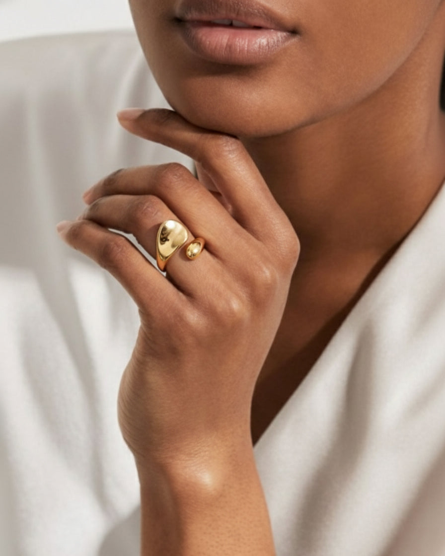 Close-up of a hand wearing a gold ring with a heart design on a neutral background