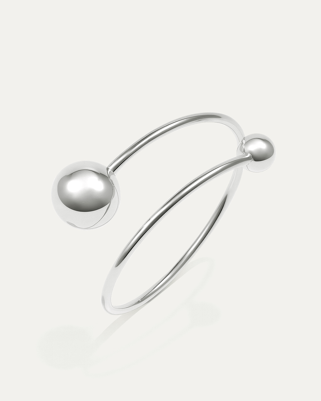 A silver cuff bracelet with a minimalist, open design. It features a smooth, thin band that wraps around, ending in two polis