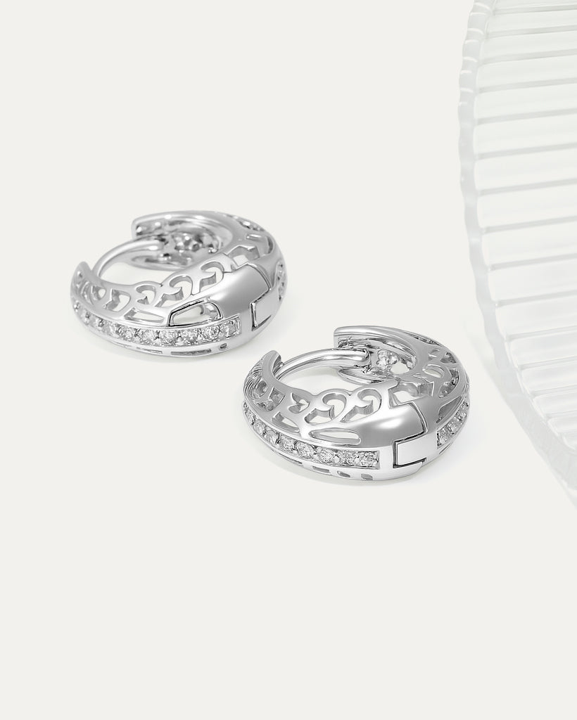 Pair of silver hoop earrings with intricate designs on a light gray background