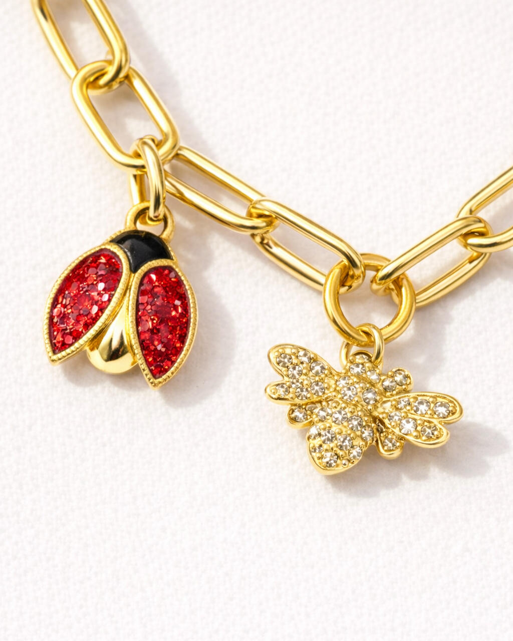 Close-up of an 18K gold-plated charm necklace featuring a bold chain with ladybug and bee charms, detailed crystal accents by