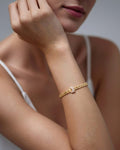 A close-up of a woman's arm wearing a gold-plated chain bracelet with a statement equestrian-style clasp. The bracelet featur