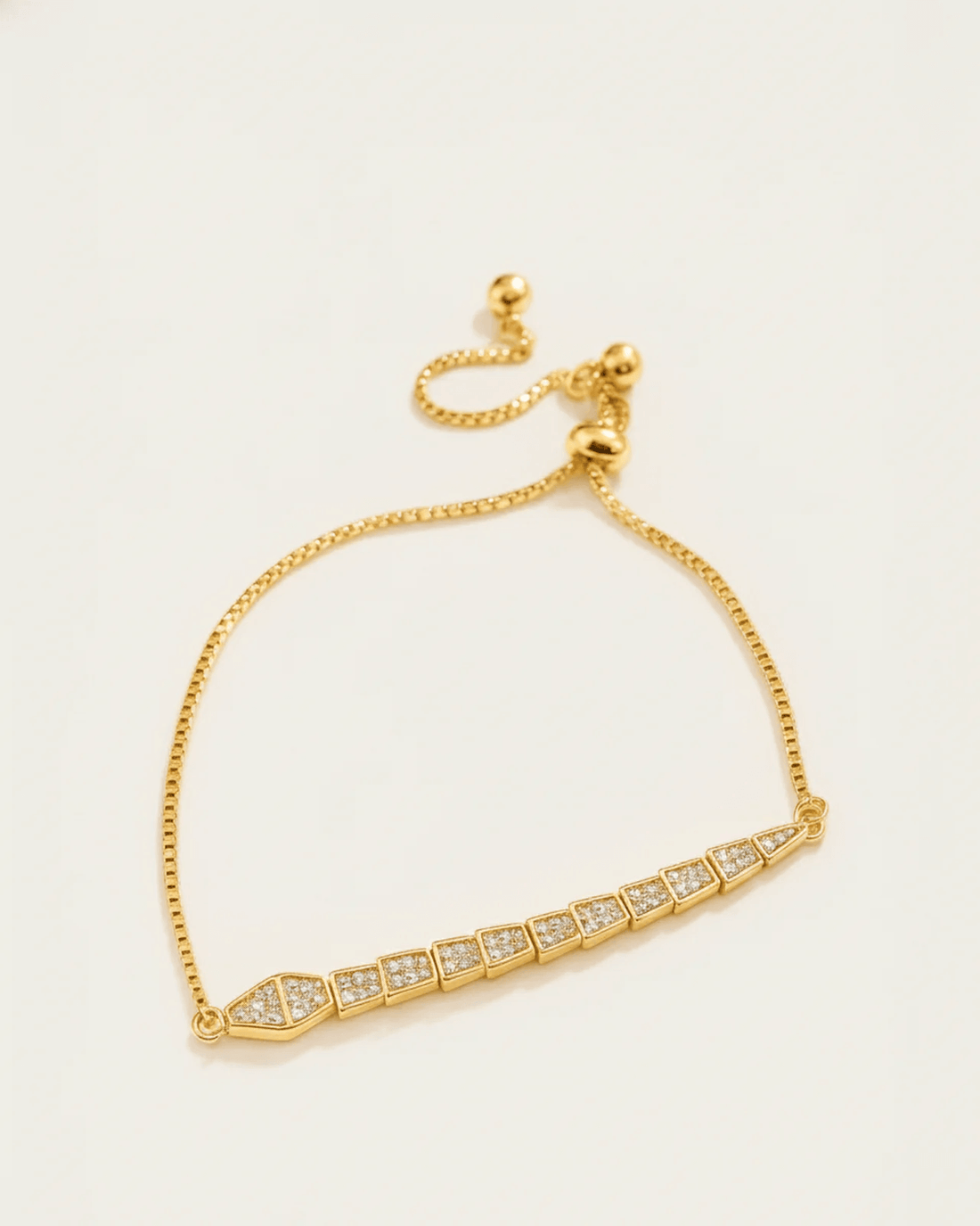 A gold-plated slider bracelet with a delicate chain and a serpentine, geometric centerpiece. The adjustable bracelet features
