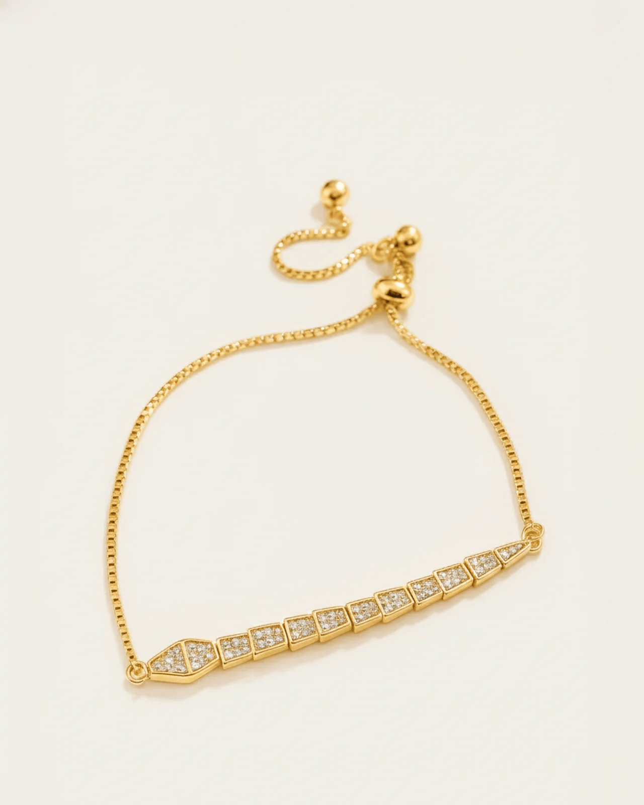 A gold-plated slider bracelet with a delicate box chain and an adjustable ball closure. The centerpiece is a serpent-like bar