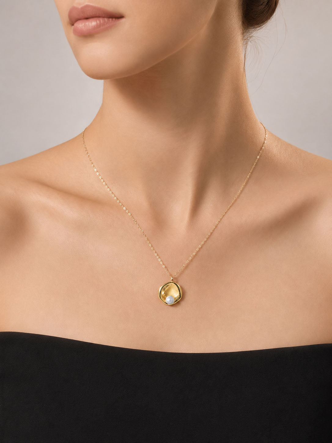 Gold necklace with a pendant featuring a pearl on a light beige background
