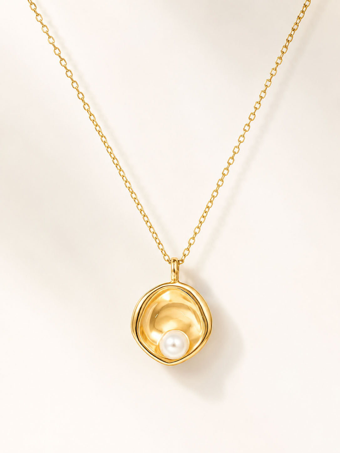 Gold necklace with a pendant featuring a pearl on a light beige background
