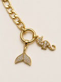 Gold bracelet with a mermaid tail and elephant charm on a beige background
