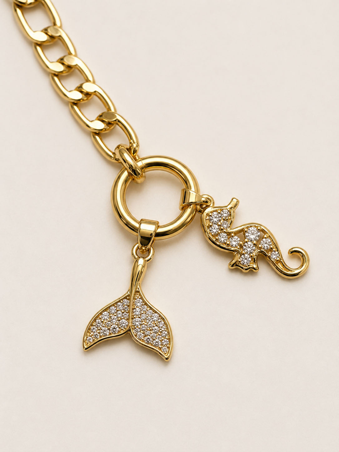 Gold bracelet with a mermaid tail and elephant charm on a beige background