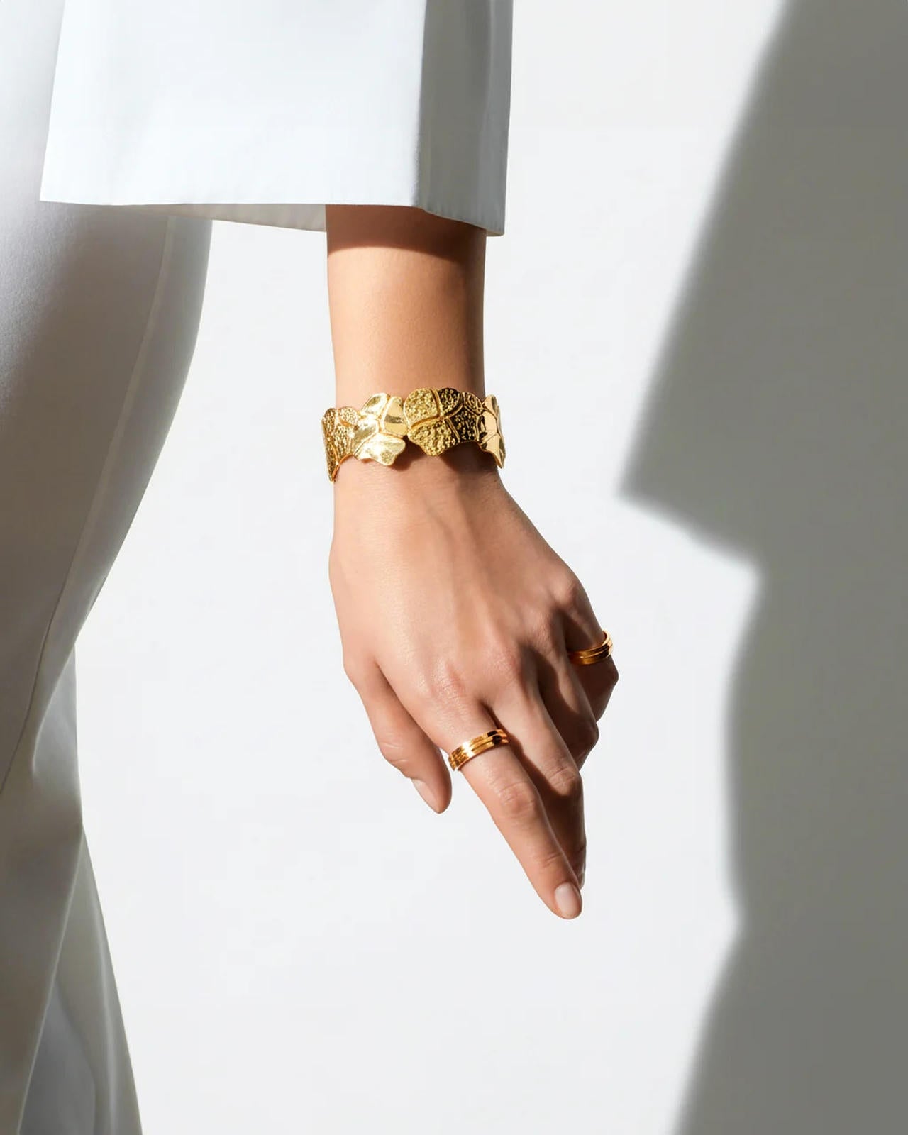 Hand wearing gold bracelets and rings on a white background