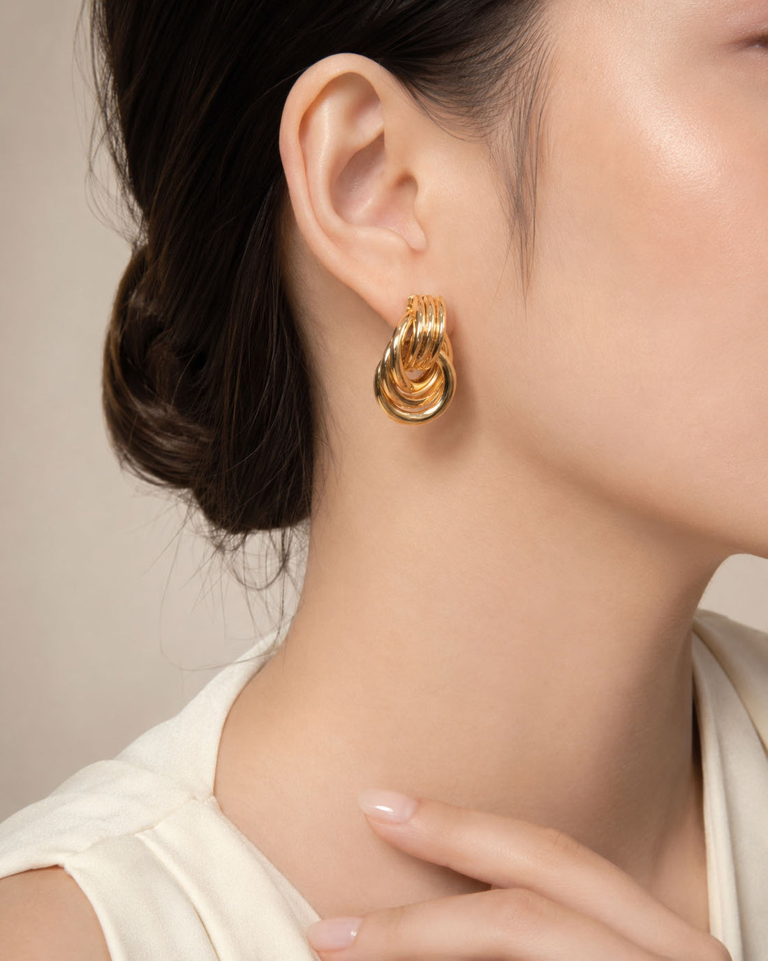 Gold knot earrings on a light beige background