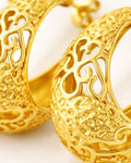 Close-up gold-plated crescent hoop earrings with ornate baroque cutout texture