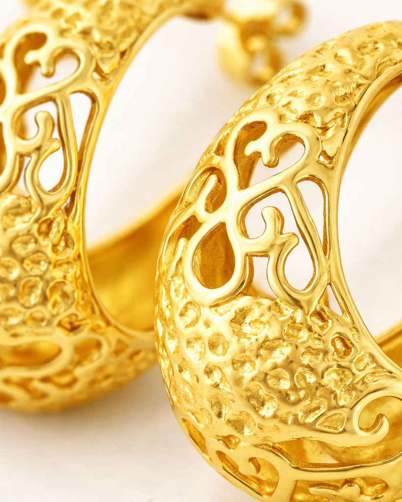 Close-up gold-plated crescent hoop earrings with ornate baroque cutout texture