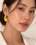 Model wearing gold-plated crescent hoop earrings with baroque cutout design