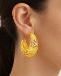 Model wearing gold-plated crescent hoop earrings with ornate cutout design