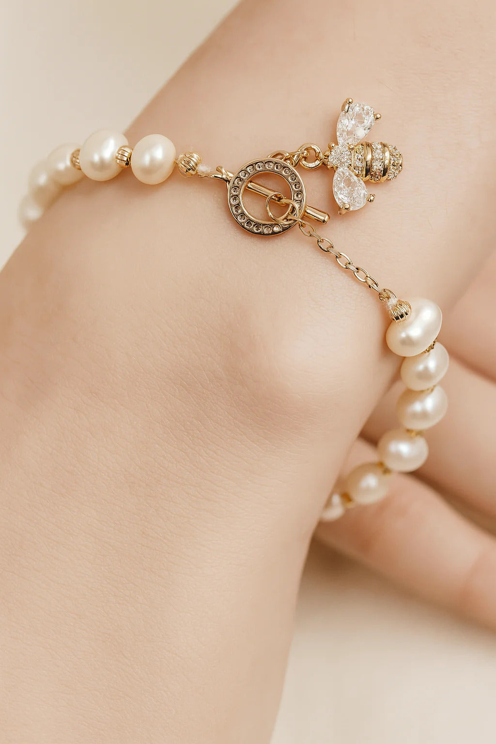 Pearl beaded bracelet worn on model, featuring a gold bee charm and toggle clasp with crystal details by Jadejuri