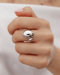 A close-up of a hand wearing a bold silver open-cuff ring on the middle finger. The statement ring features two polished, con