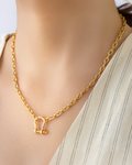 Gold chain necklace with bold D-shackle pendant worn with light striped fabric.