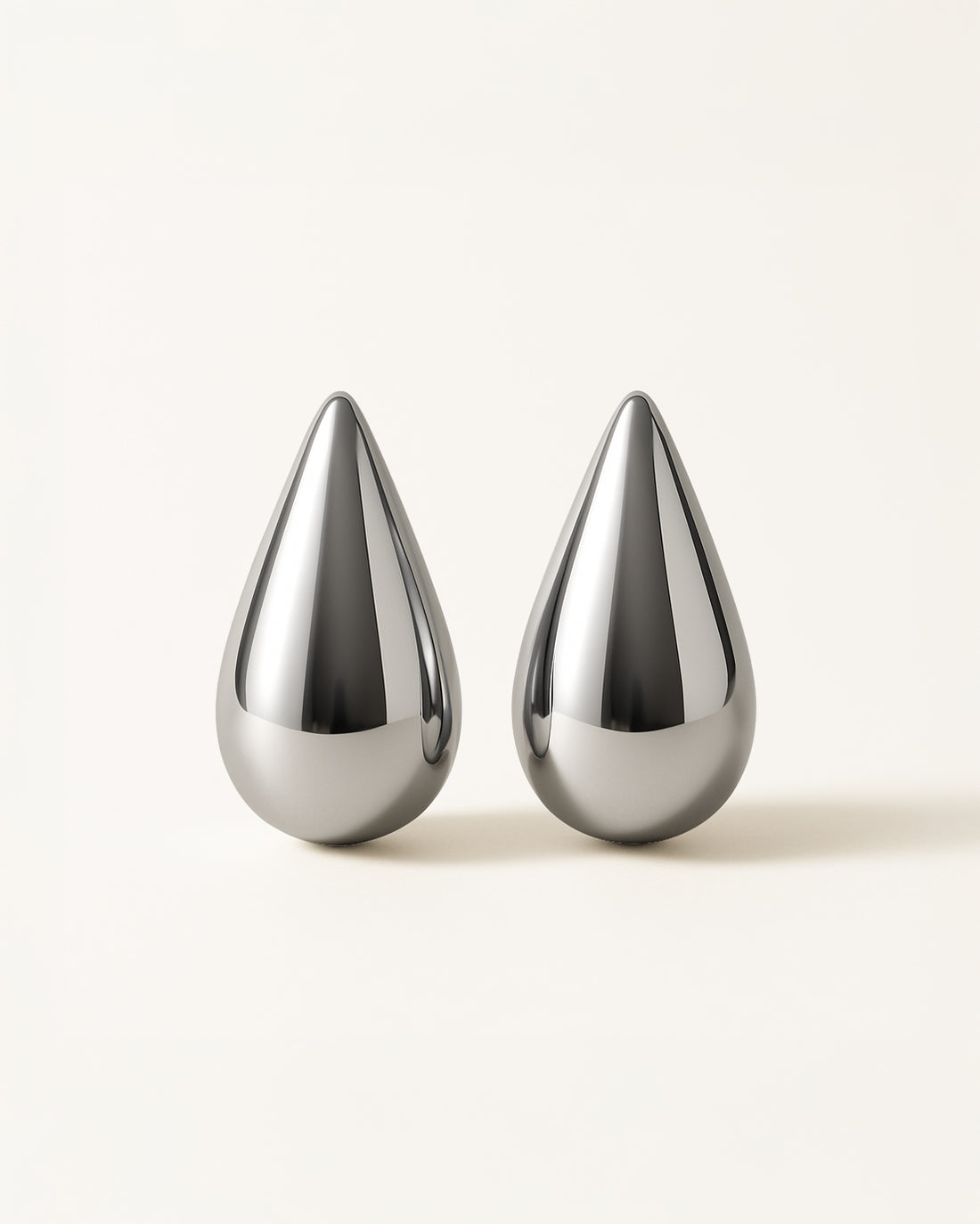 A pair of silver bold teardrop stud earrings with smooth sculptural surface, displayed against a soft neutral background.