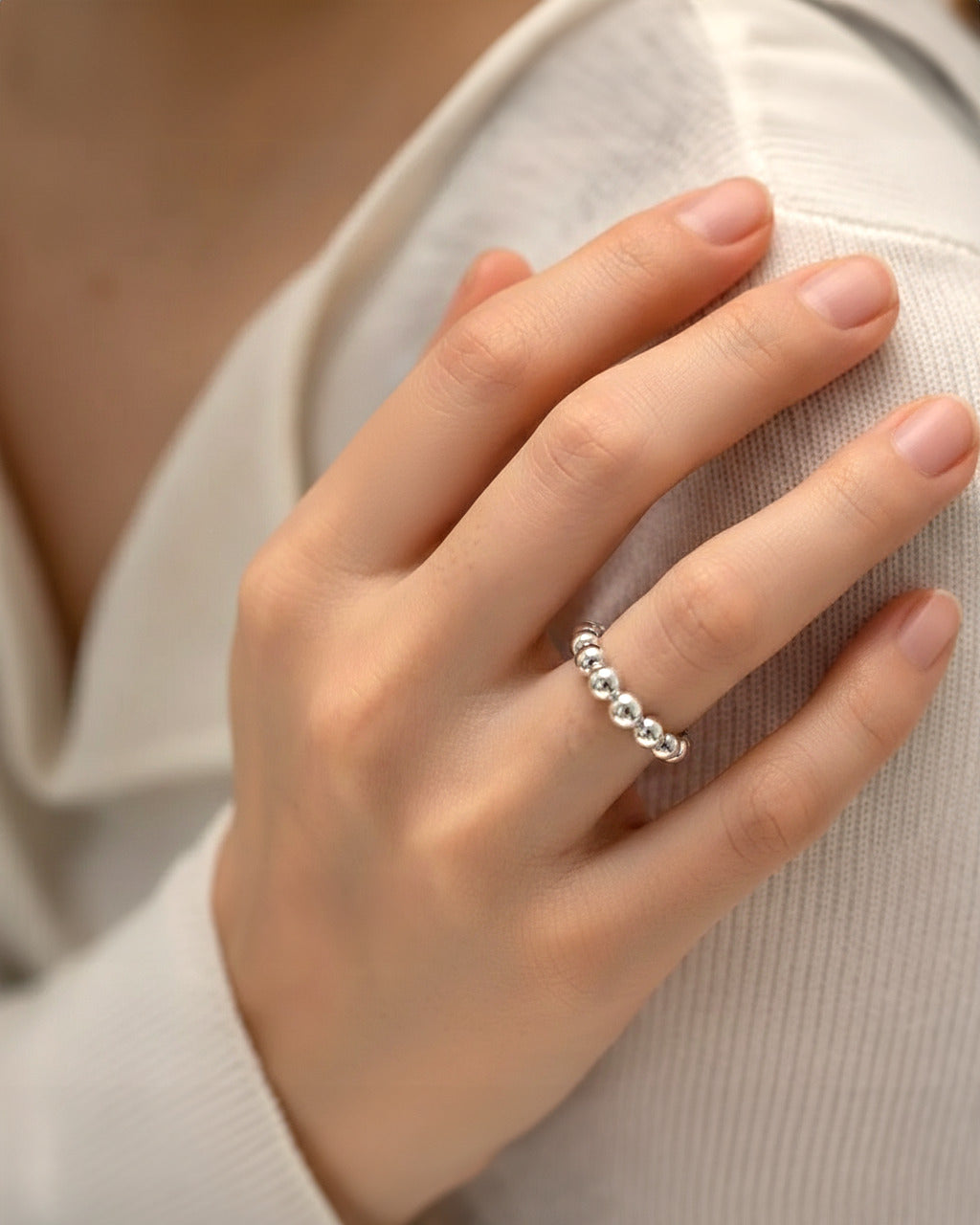 A close-up studio shot of a silver-tone cuff ring on a plain white or light beige background. The ring has an adjustable, ope