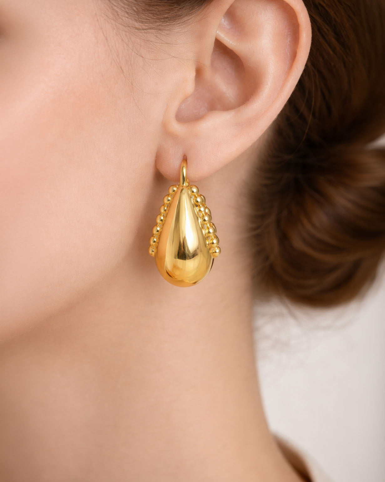 Gold teardrop earrings with beaded detail worn on ear minimalist jewelry