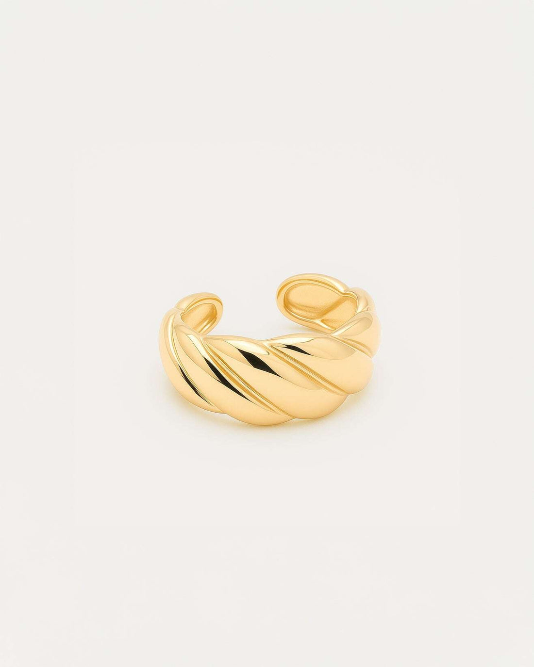 A close-up studio shot of a chunky, adjustable gold-tone cuff ring on a plain white or light beige background. The band featu