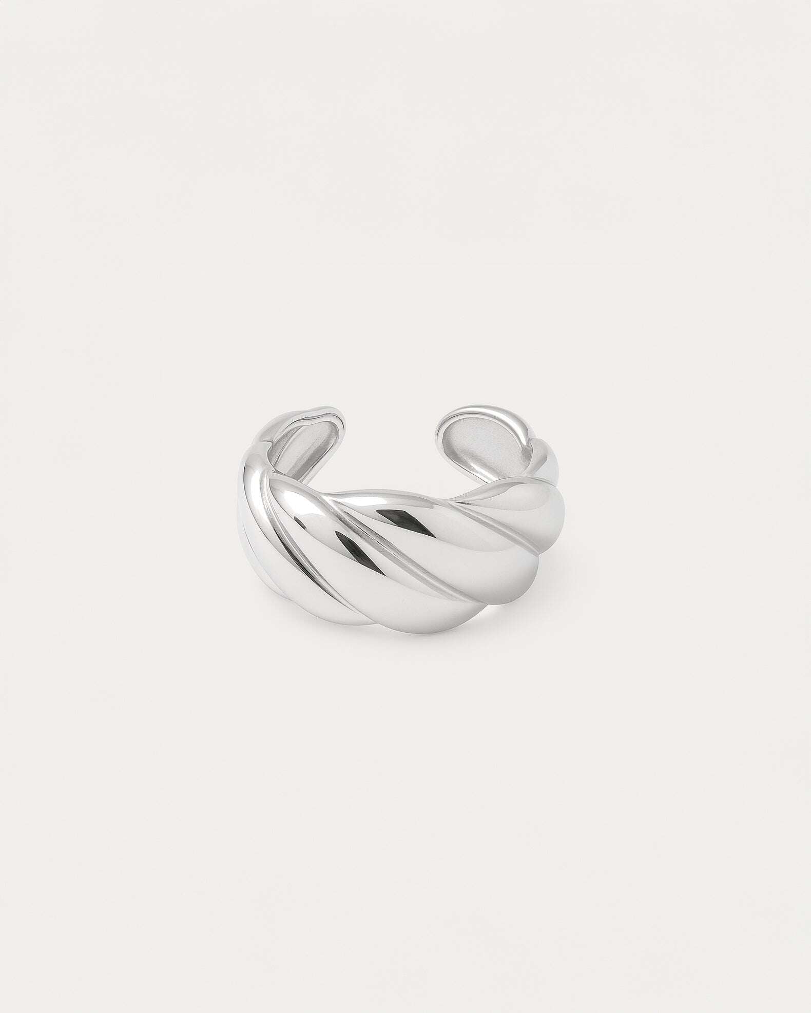A close-up studio shot of a chunky, adjustable silver-tone cuff ring on a plain white or light beige background. The band fea