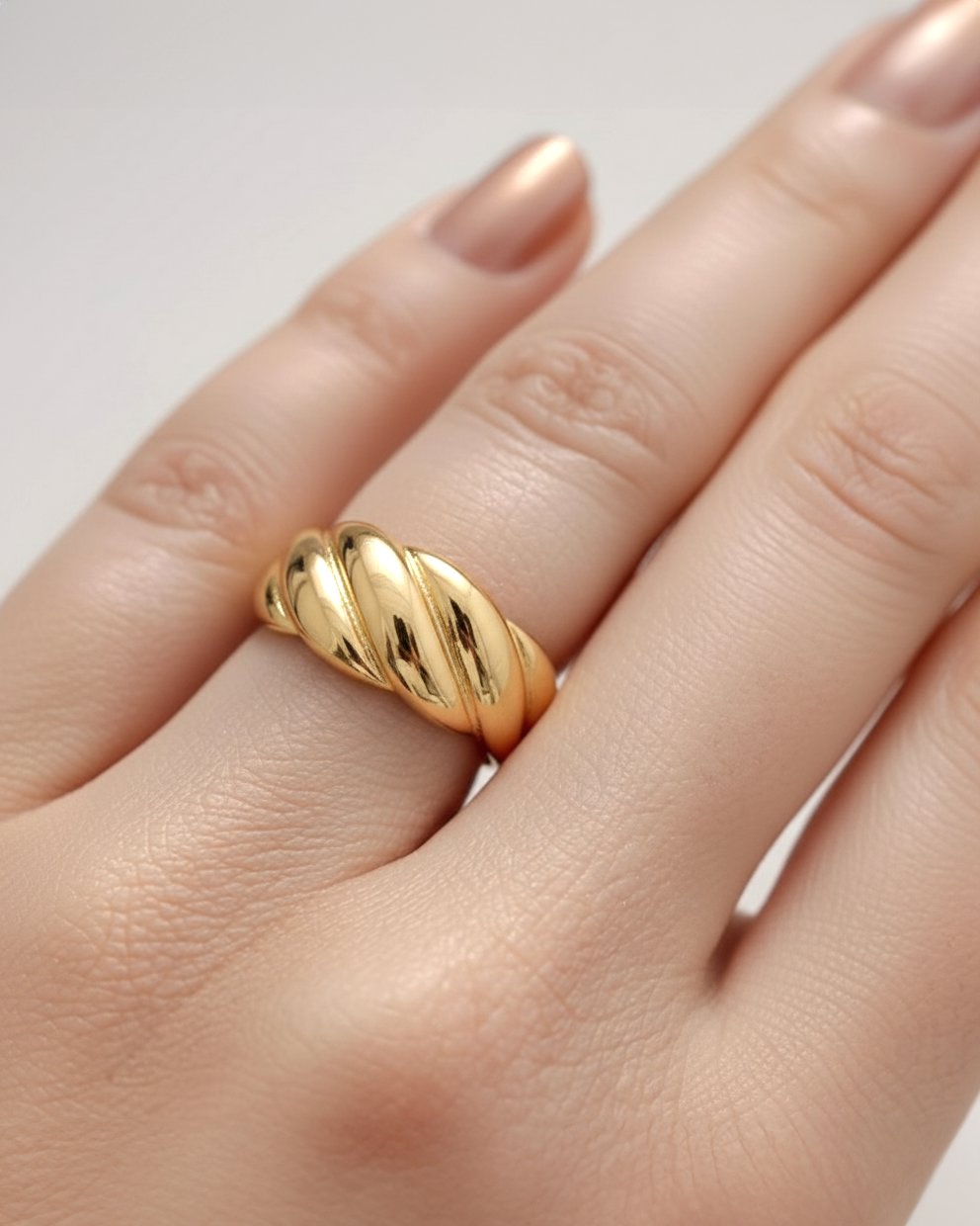 A close-up studio shot of a chunky, adjustable gold-tone cuff ring on a plain white or light beige background. The band featu