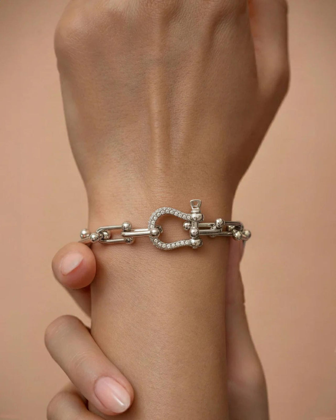 A silver-plated bracelet with polished rectangular chain links and a D-shaped clasp encrusted with pavé crystals, worn on a person's wrist.