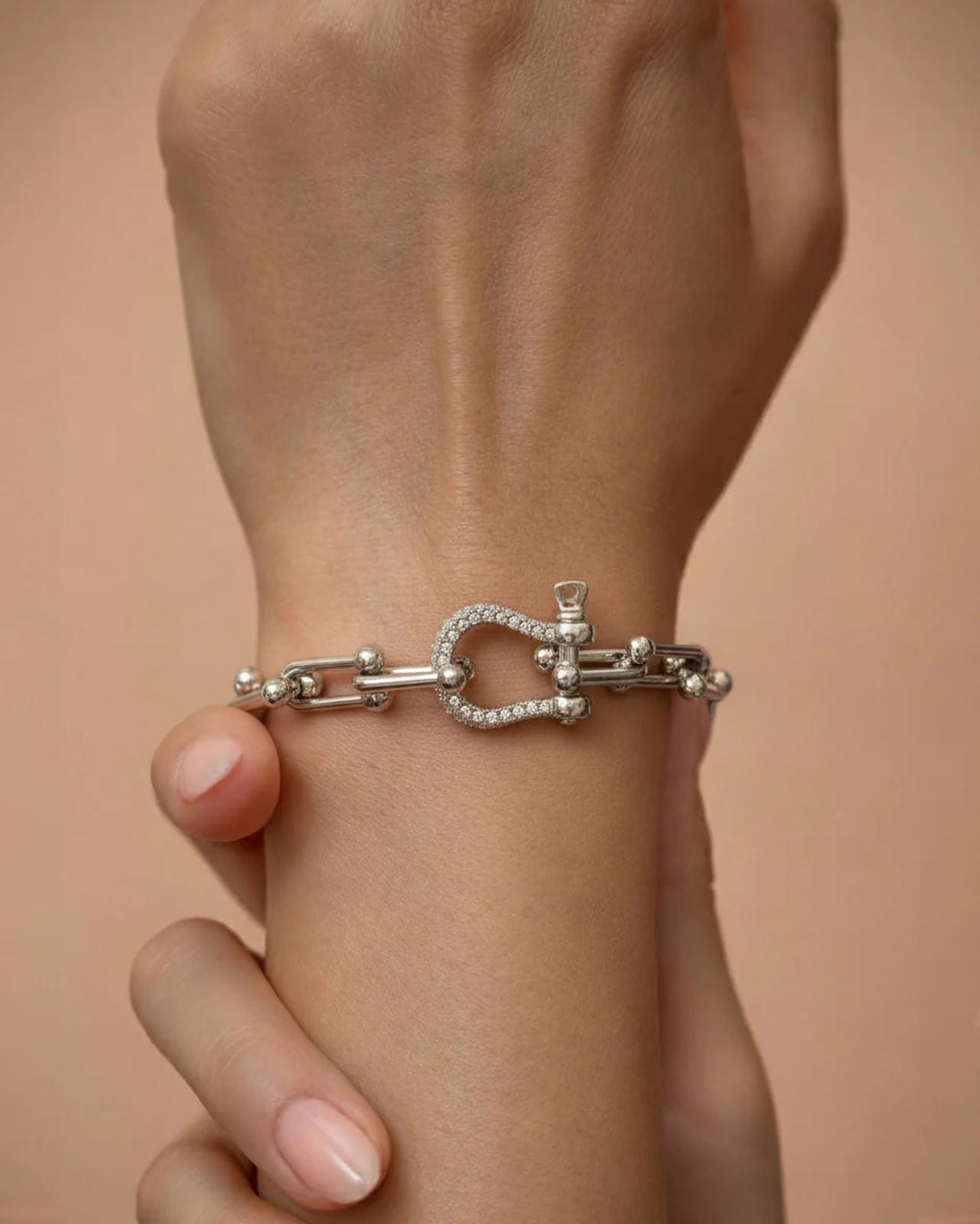 A silver-plated bracelet with polished rectangular chain links and a D-shaped clasp encrusted with pavé crystals, worn on a person's wrist.