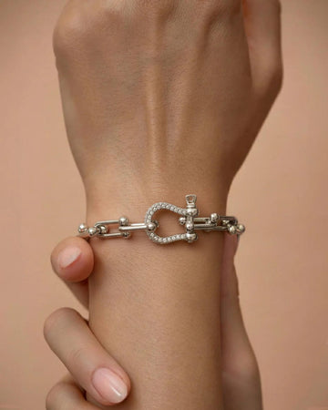 A silver-plated bracelet with polished rectangular chain links and a D-shaped clasp encrusted with pavé crystals, worn on a person's wrist.