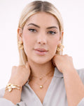 Model wearing 18k gold-plated DNA helix hoop earrings, sculptural twisted design, styled with layered gold necklaces and brac