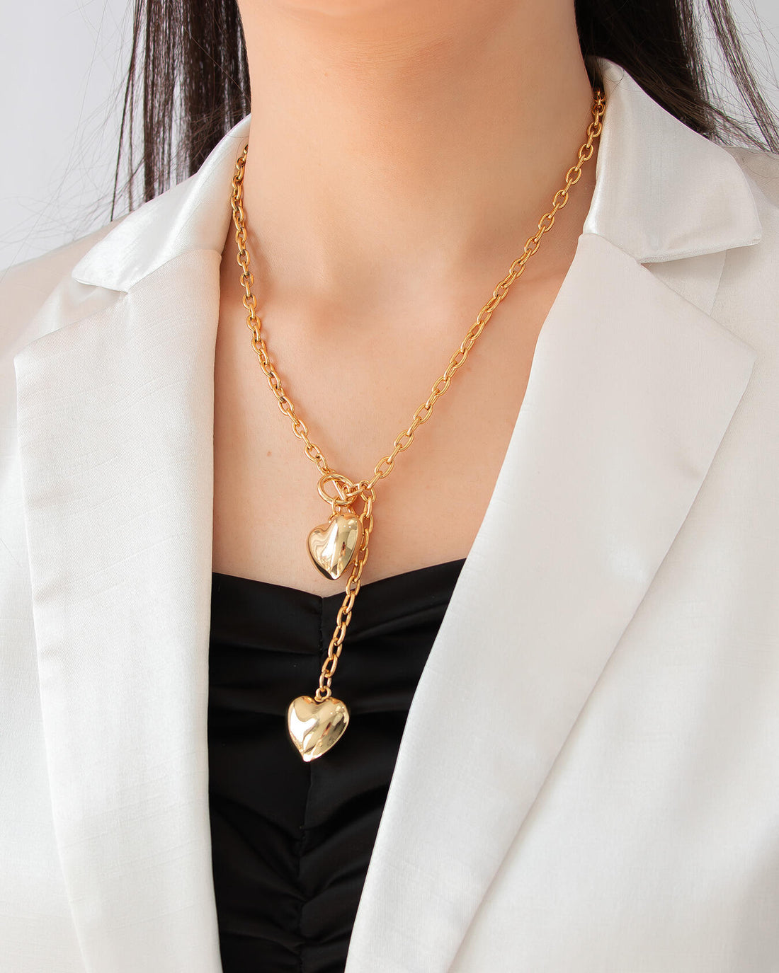 Model wearing gold lariat necklace with double heart pendants and polished 18K gold finish