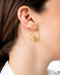 Gold sculptural drop earrings with overlapping loops and sphere accents, worn on model.