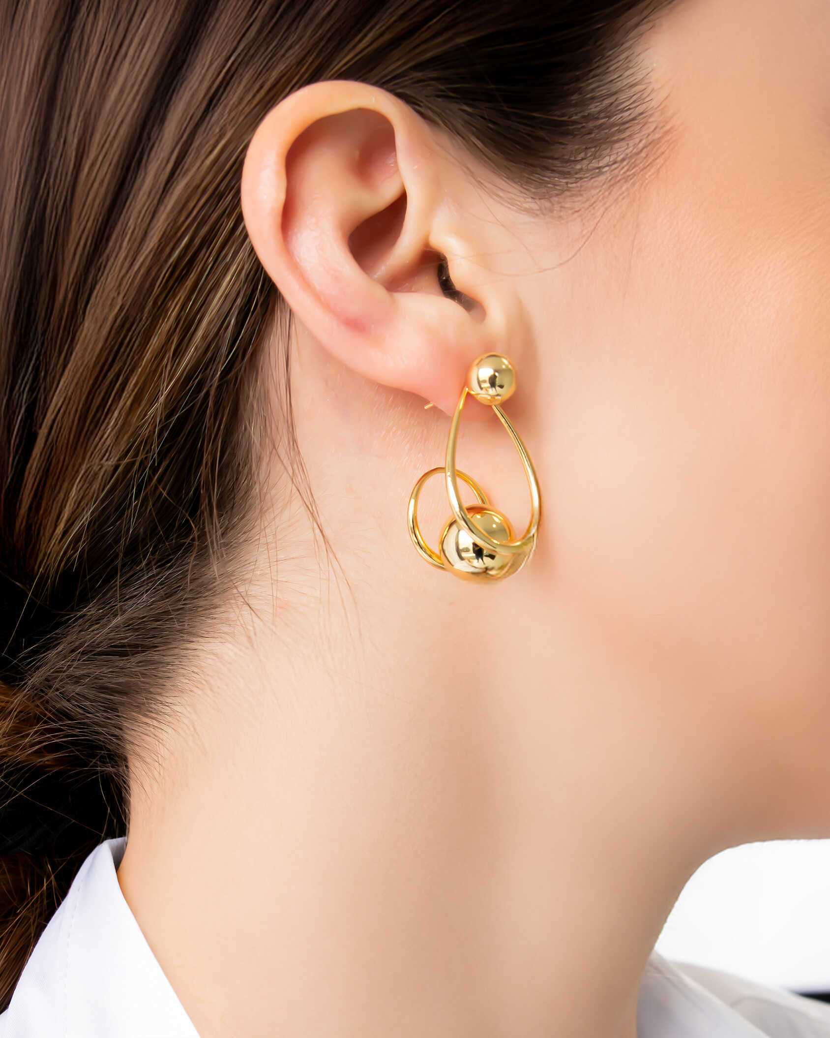 Gold sculptural drop earrings with overlapping loops and sphere accents, worn on model.