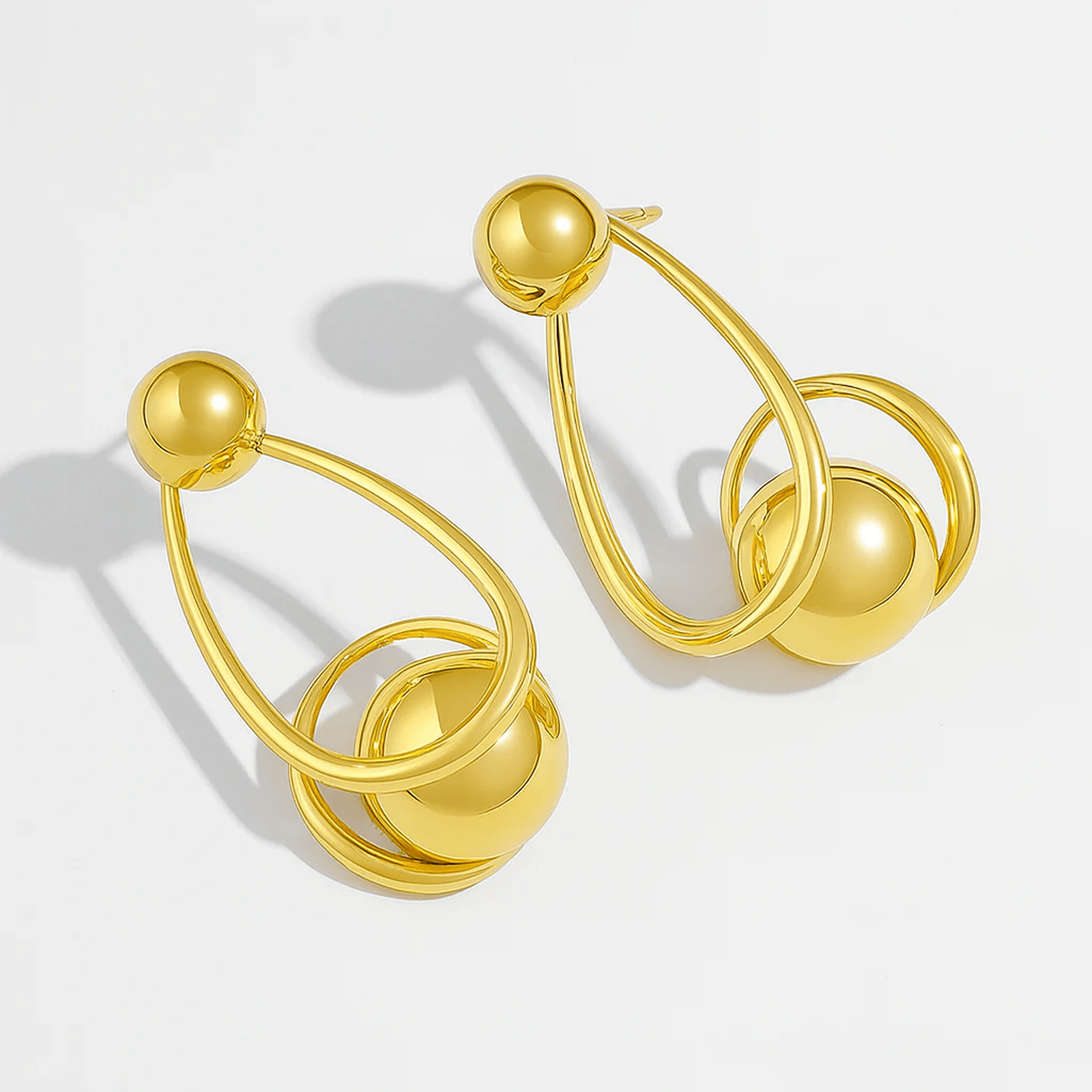Gold hoop earrings with spherical ends on a light gray background
