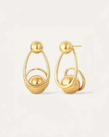 Gold sculptural drop earrings with overlapping loops and sphere accents, worn on model.